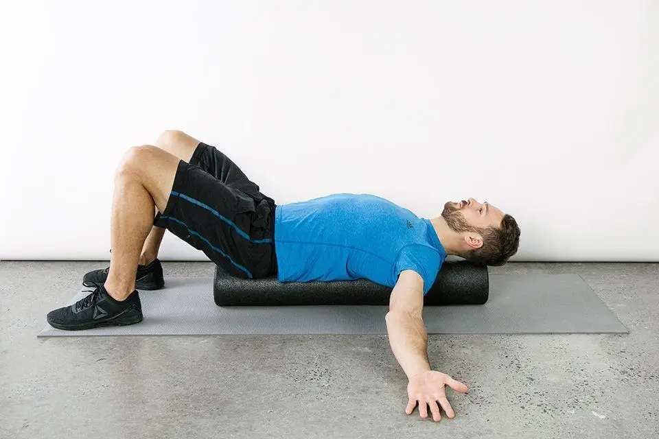 a man, arms outstretched and knees bent, lying on is back on a foam roller