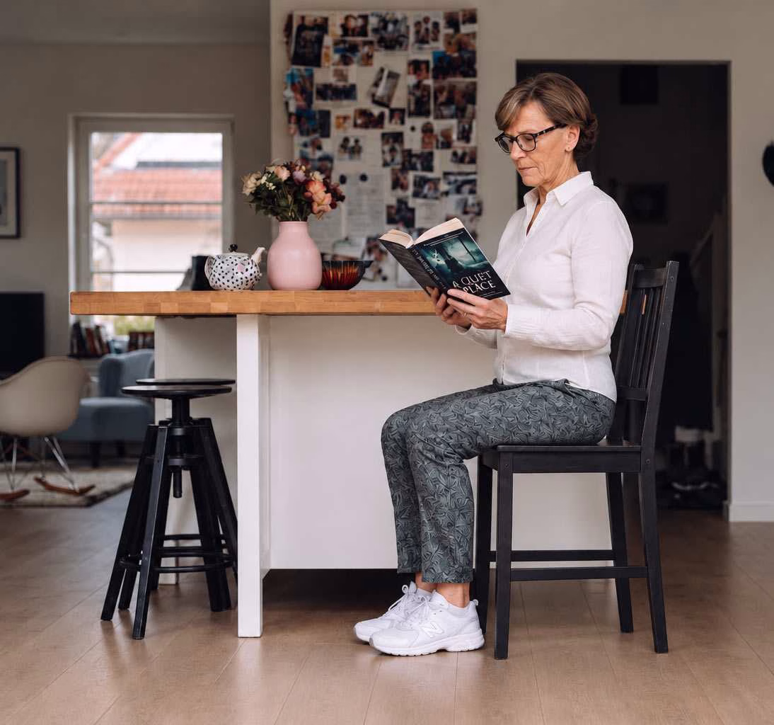 a woman sits upright in her kitchen chair, reading a book - she knows that good posture can help with her sciatica pain